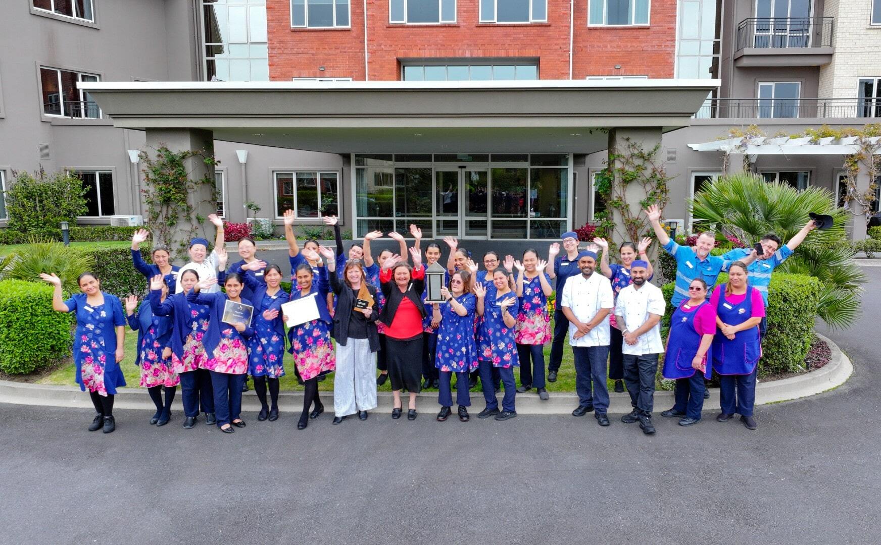 Large group of people standing in front of retirement village holding awards and celebrating