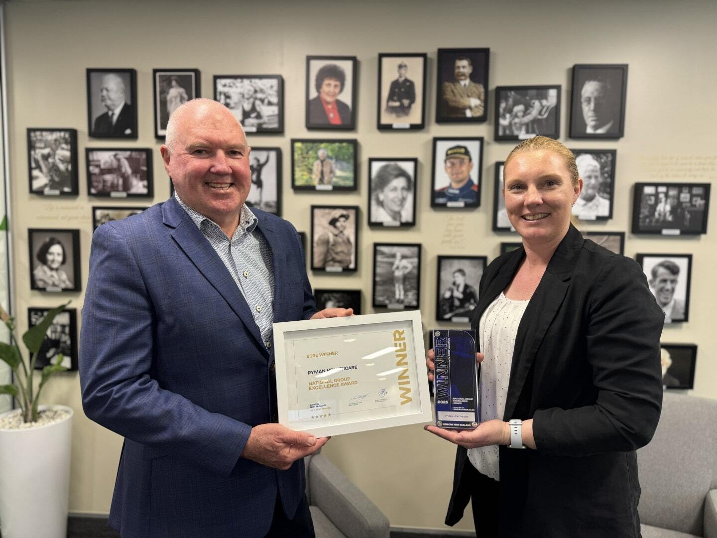 Smiling man in suit receives framed award from smiling woman